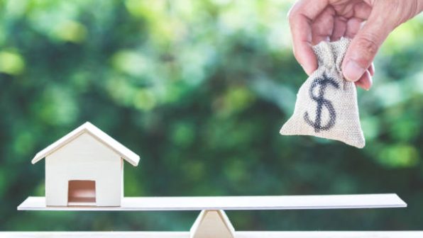 1655117191_istockphoto-1048402108-612×612 Balance home and money, home loan, reverse mortgage concept : A man hand put us dollar money bag into scales on table with green nature as background. Savings, investment, loan for plan in the future.