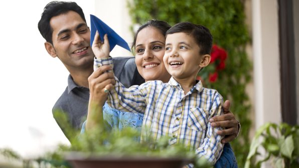 Indian family playing with paper airplane Happy parents with son throwing paper airplane in air